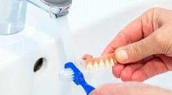 Patient cleaning dentures with soft-bristled brush